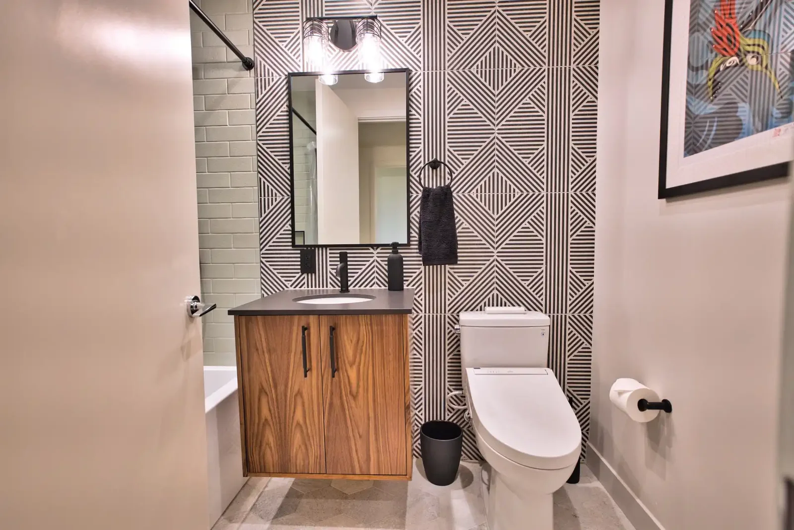 Small bathroom with a walnut floating vanity, graphic tiled feature wall and a black-framed mirror &mdash; East Avenue remodel in Austin by Bailey & Bear Construction