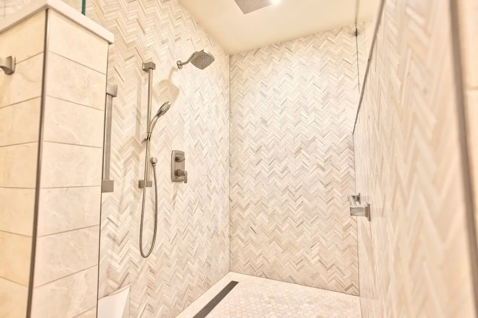 Curbless walk-in tile shower with herringbone marble walls, a linear drain and frameless glass, built by Bailey & Bear Construction on the East Avenue remodel in Austin