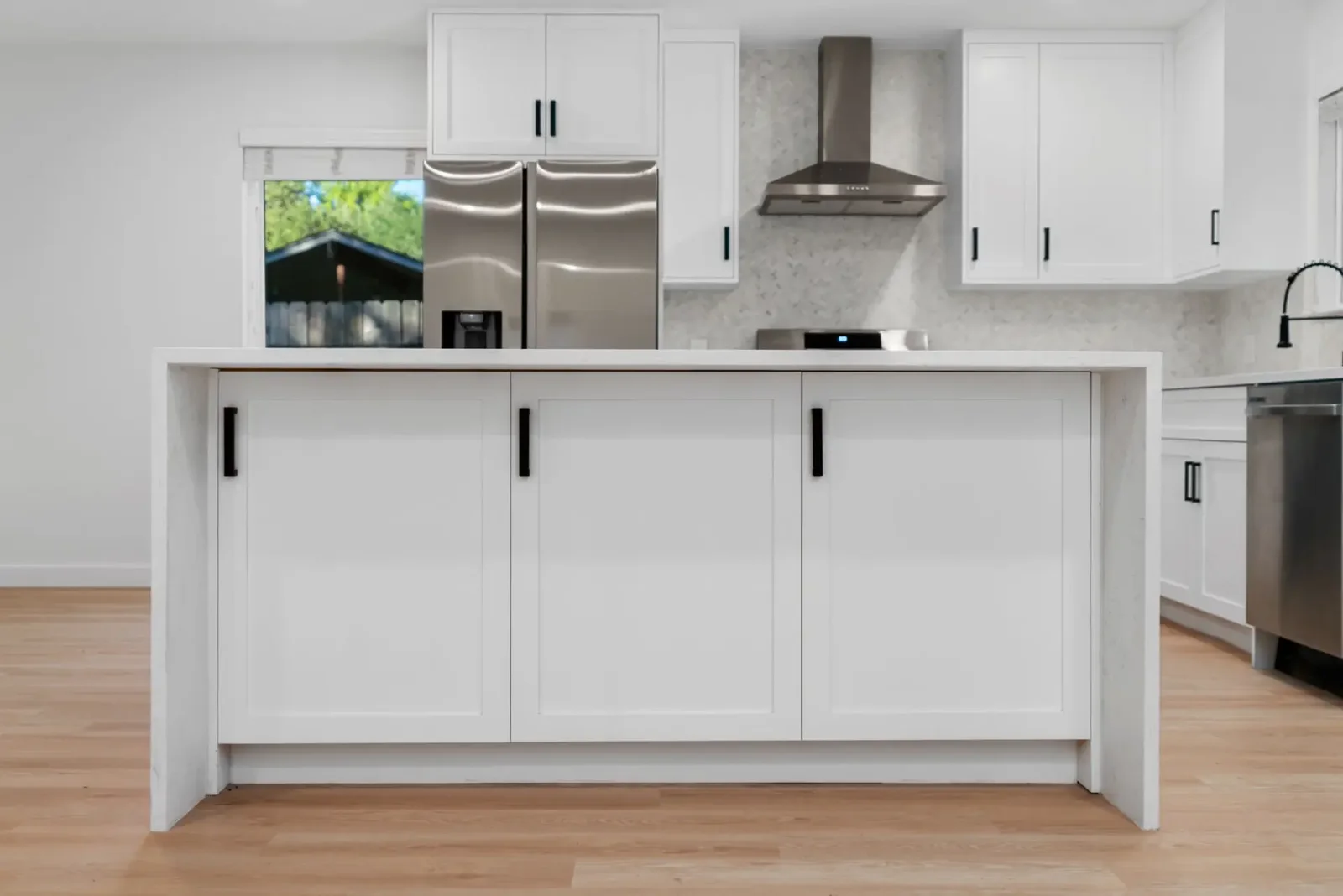 Open-plan kitchen with a large waterfall-edge island and stainless refrigerator &mdash; Emerald Forest remodel in Austin by Bailey & Bear Construction